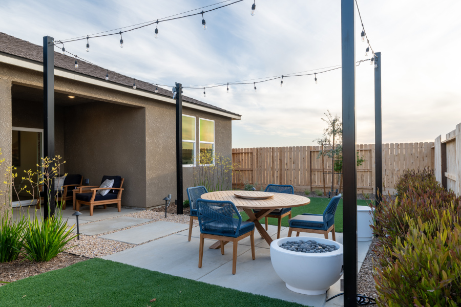 A backyard with a table chairs and a patio with a fence and a house.