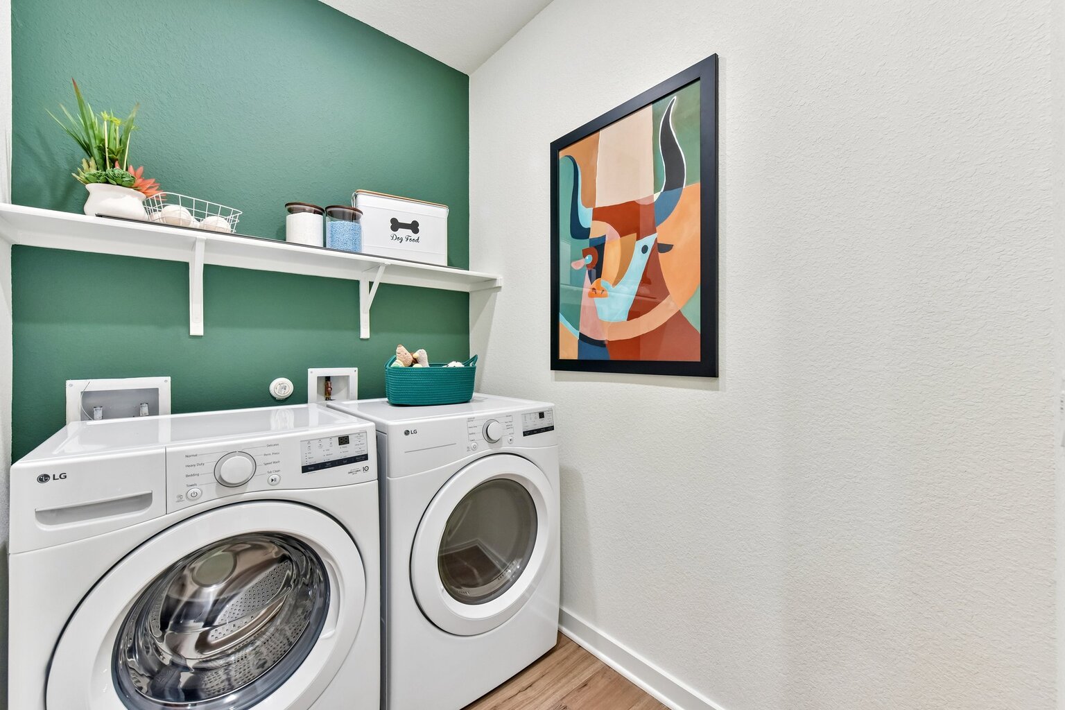 A room with a washing machine and a painting on the wall.