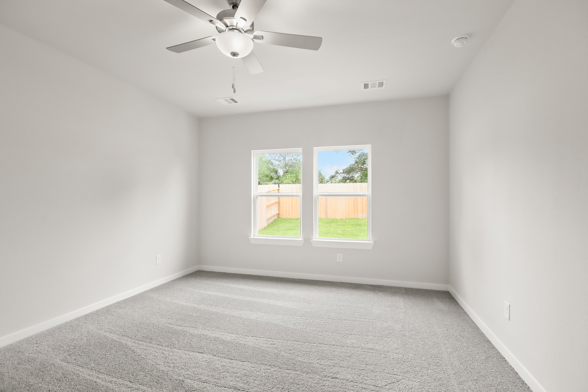 A room with a ceiling fan and a window with a view of the yard.