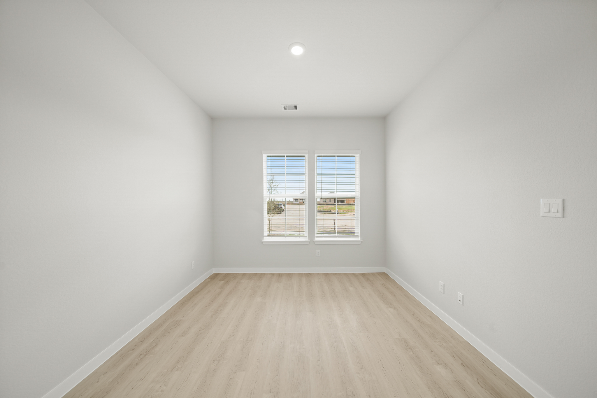 A room with a wood floor and a window with blinds.