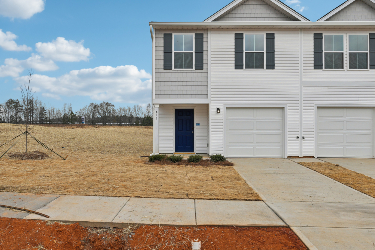 A house with a garage and dirt in front of it.